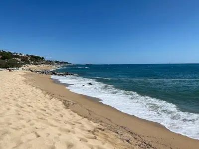 a sandy beach with the ocean on a sunny day at Bright airy family style 7 min walk to beach in Caldes d'Estrac