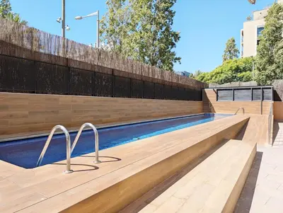 a swimming pool with a wooden retaining wall and a fence at Bright 2 Bedroom Apartment with 2 Terraces Pool and Parking near Diagonal Mar Beach in Sant Adria de Besos