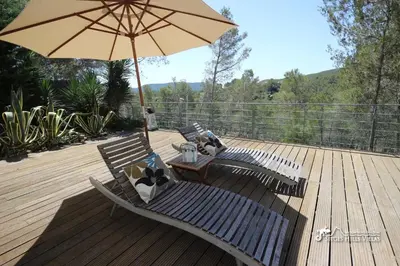 a patio with two chairs and an umbrella on a deck at Villa Lucere with private pool near Sitges in Olivella