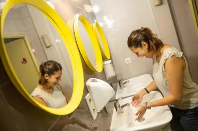 a woman washing her hands in a bathroom mirror at HeyLola! Hostel in Barcelona