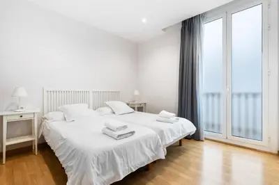 a white bedroom with a bed and a large window at Flateli Pelayo H2 in Barcelona