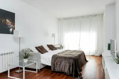 a white bedroom with a bed and a table at Glasir Homes Barcelona in Barcelona