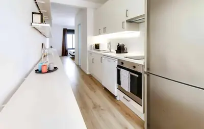 a kitchen with white appliances and a wooden floor at Urban Flats Park Guell in Barcelona