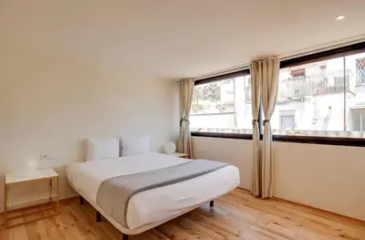 a white bedroom with a bed and two windows at Urban Flats Park Guell in Barcelona