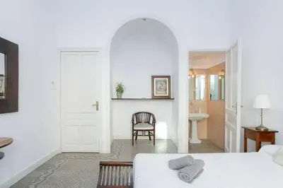 a white bedroom with a bed and a chair at Canela Homes BARCELONA CASA SERRA in Barcelona