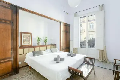 a bedroom with a large white bed and a chair at Canela Homes BARCELONA CASA SERRA in Barcelona