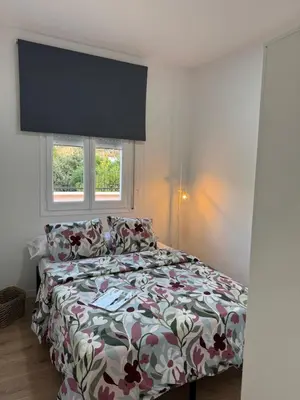 a bedroom with a bed with a floral comforter and two windows at Ático gran terraza cerca BCN in Castelldefels