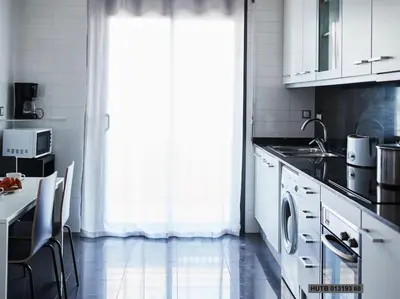 a kitchen with white cabinets and a table and a window at Alcam Cervantes Playa Badalona in Badalona