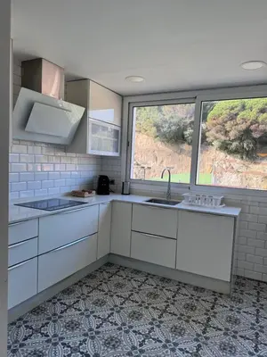 a kitchen with white cabinets and a large window at Caldetas relax apartment in Sant Vicenç de Montalt