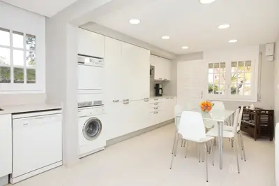 a white kitchen with a table and a washing machine at Villa Gaudi in San Justo Desvern