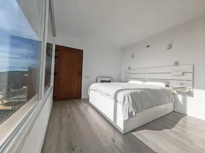 a white bedroom with a bed and a large window at Apartamento con vistas al mar in Viladecáns
