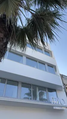 a white building with windows and a palm tree at MYO Barcelona Hotel & Apartments in Castelldefels