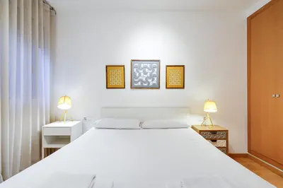 a white bedroom with a large bed and two lamps at Gran Via City Center Apartment in Barcelona