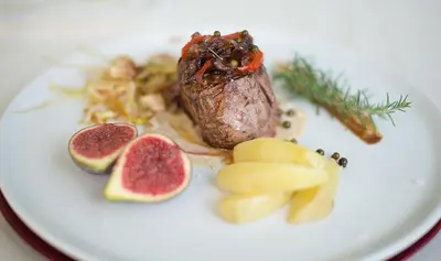 a plate of food with a piece of meat and fruit at Hotel Boutique Edelweiss La Garriga in La Garriga