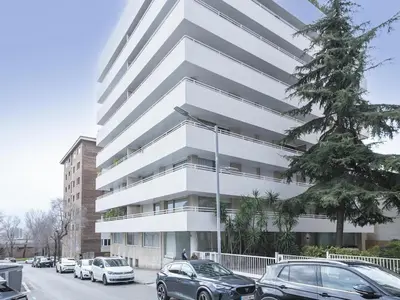 a tall white building with cars parked in a parking lot at Winahost Barcelona Pedralbes in Barcelona