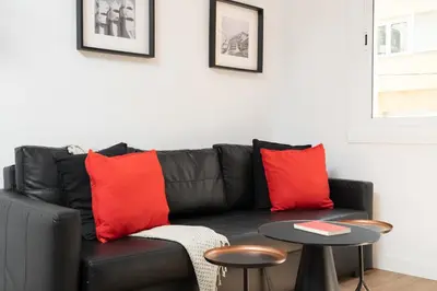 a black leather couch with red pillows and a table at Dúplex Deluxe Apartment in Badalona