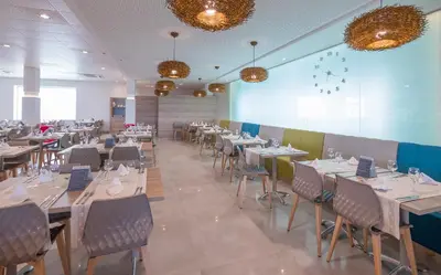 a restaurant with tables and chairs in a room at Golden Taurus Aquapark Resort in Pineda de Mar
