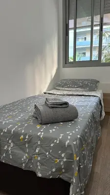 a bed with a gray comforter and a window at Apt compartido martirrena in Badalona