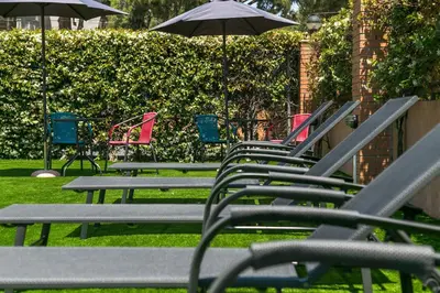 a row of lawn chairs with umbrellas in the grass at Aparthotel Bardon in Castelldefels