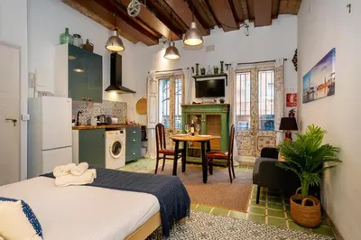 a room with a bed and a kitchen with a table at Estudios a 10' caminando de la playa y a 20' de Barcelona Centro in Sant Adria de Besos
