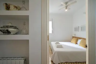 a white bedroom with a bed and a ceiling fan at Habitat Apartments Vila in Barcelona