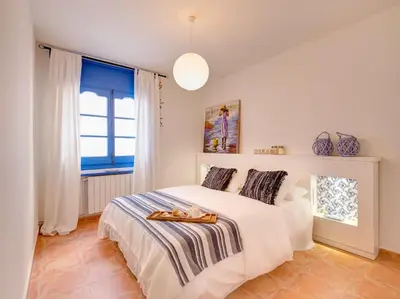a white bedroom with a bed and a window at Blue Home in Sitges