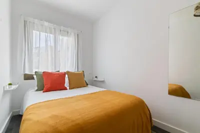 a bedroom with a bed with orange sheets and a window at Toledo House Self Checkin in Hospitalet de Llobregat