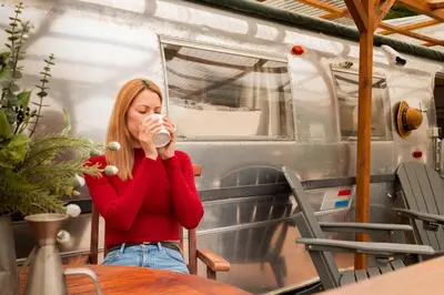 a woman sitting at a table drinking from a cup at Caravana Airstream Vintage del 67 en Orrius, Barcelona in Orrius