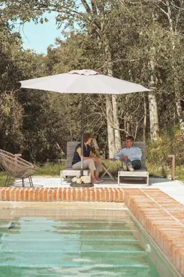 two people sitting under an umbrella next to a pool at Paratgea in Llinars del Vallès