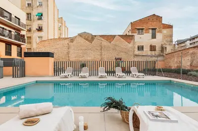 a swimming pool with chairs and a table and a building at Heures - 2 bedroom, office and pool in Les Corts in Barcelona