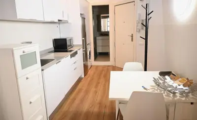a kitchen with white cabinets and a table with chairs at Homenfun Barcelona Ciutat Vella in Barcelona