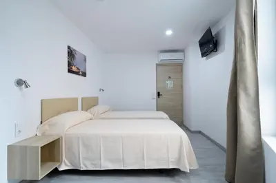 a white bedroom with two beds and a tv at Hotel Plini in Hospitalet de Llobregat