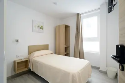 a white bedroom with a bed and a window at Hotel Plini in Hospitalet de Llobregat