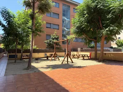 a park with a swing and benches in front of a building at Dúplex con encanto en Castelldefels in Castelldefels