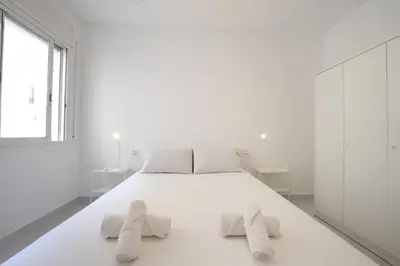 a white bedroom with a large white bed with two towels at Winahost Barcelona Sants in Barcelona
