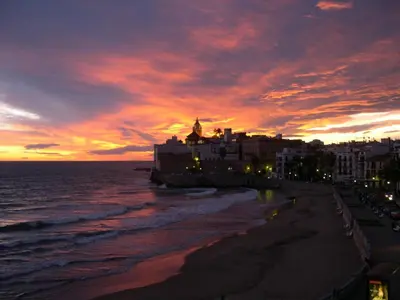 a sunset over a beach with a building and the ocean at Rustic good in Sitges