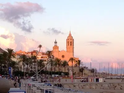 a building on the beach with palm trees in front of it at Ático con vistas al mar, solarium privado y piscina in Sitges