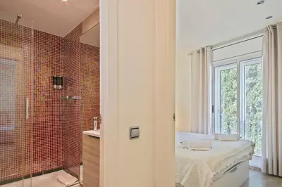 a bathroom with a shower and a bed and a window at Beach Penthouse in Sitges