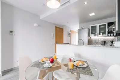 a white kitchen with a glass table and chairs at Weflating Barcelona Sants in Barcelona