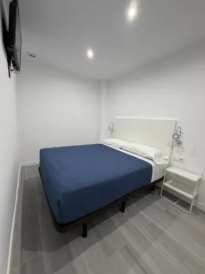 a bed in a white room with a blue blanket at Hostel Hock Residences in Hospitalet de Llobregat