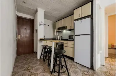 a kitchen with a white refrigerator and bar stools at Apartamento en Barcelona Pau sans in Hospitalet de Llobregat