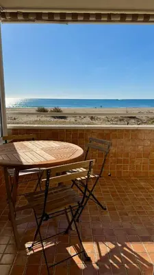 a wooden table and a chair sitting next to a beach at Apartamento precioso en primera línea de mar in Les Botigues de Sitges