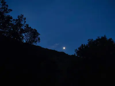 the moon rising over a hill at night at El Roserar Cabaña de Madera y Caravana Vintage Parque Natural del Montseny in Montseny