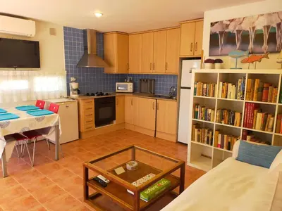a living room with a table and a kitchen at Lovely little house with garden in Sant Vicenç de Montalt