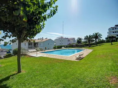 a swimming pool in a grassy yard with a tree at Viva Palms by Hello Homes Sitges in Sitges