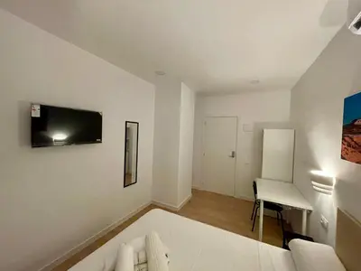 a living room with a couch and a tv on the wall at Lux Hostal in Hospitalet de Llobregat