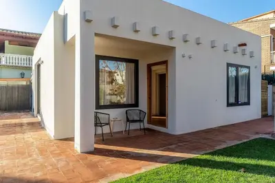 a white house with a patio with two chairs at Canela Homes COSTA LA PINEDA in Castelldefels