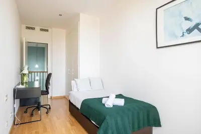 a bedroom with a bed with a green blanket and a desk at Homenfun Barcelona Fira Gran Via in Hospitalet de Llobregat