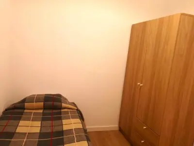 a bed with a plaid blanket next to a wooden cabinet at ApartEasy mid-term ONLY for VACATIONS stays, BORRELL in Barcelona