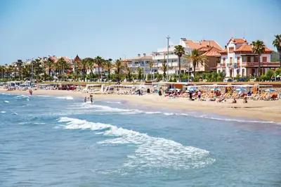 a beach with a group of people sitting on the sand at Francesc Macià, Sitges in Sitges